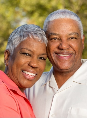 Senior man and woman grinning outdoors with trees in background