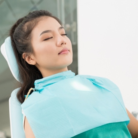 Young woman laying back in dental chair with eyes closed